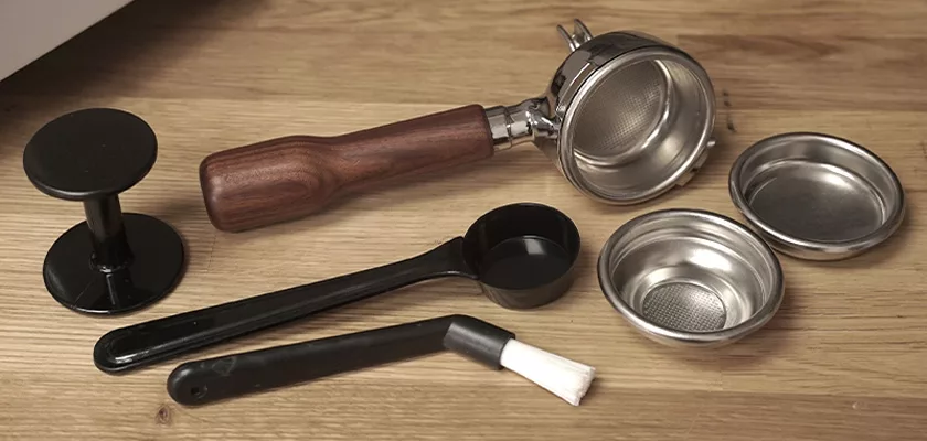 A portafilter with a wooden handle, metal filter baskets, and a black tamper on wood—perfect accessories for making espresso with your Bezzera Crema PM HX Espresso Machine. © 2025 1st-line.com