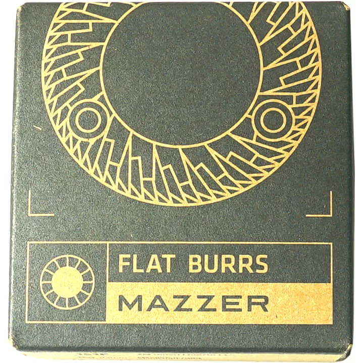 The Mazzer FMA00151F/QQQ 83mm Grinding Burr Set comes in a black and gold box with a stylized circular burr design and the text FLAT BURRS and MAZZER on the front, indicating it’s for Mazzer grinders. © 2025 1st-line.com