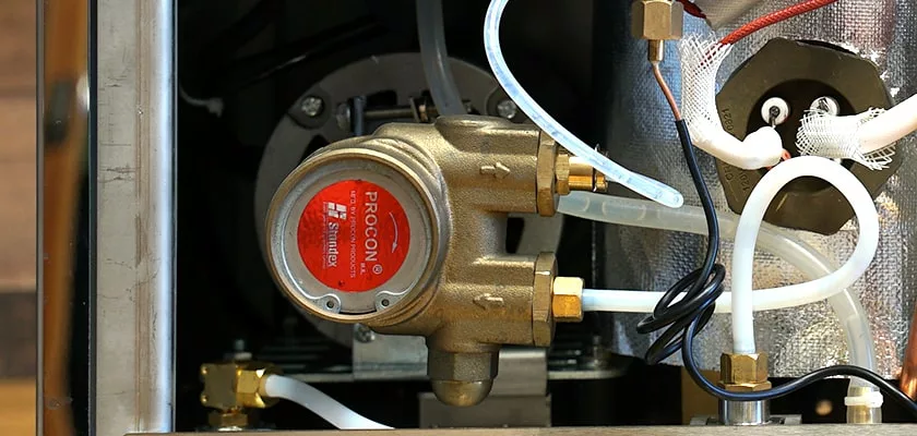 Close-up of a brass Procon rotary vane pump with white and black tubing, mounted inside a Bellezza Inizio R Leva HX Espresso Machine, with visible wiring and metal components in the background. © 2025 1st-line.com