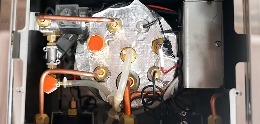 Close-up of the internal components of the Bellezza Inizio R Leva HX Espresso Machine, displaying metal pipes, copper tubing, insulated boiler, wires, connectors, and fittings. © 2025 1st-line.com
