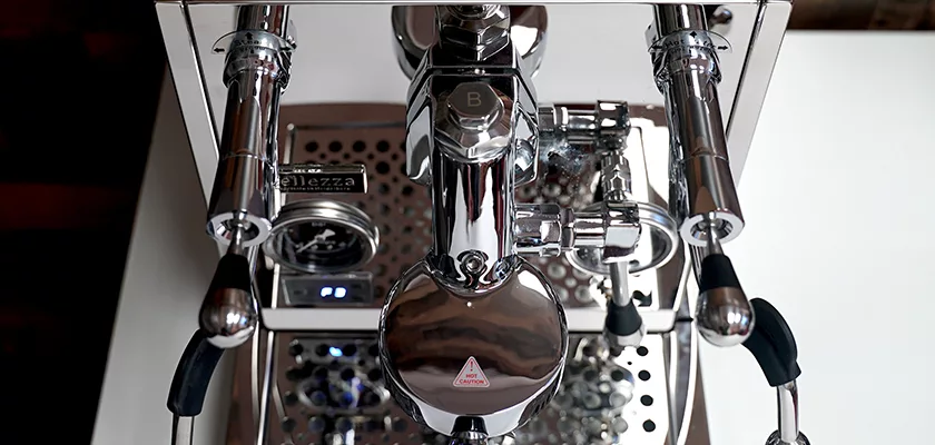 Top-down view of a shiny Bellezza Inizio R Leva HX Espresso Machine with multiple levers, knobs, and a pressure gauge; its black handles stand out on both sides as the surface reflects the surroundings. © 2025 1st-line.com