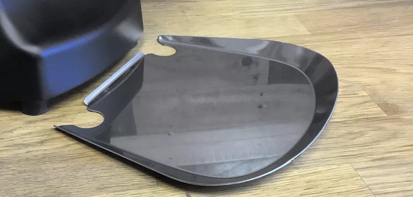 A curved, reflective black plastic tray with side notches rests on a wooden floor next to a Mazzer Kony S Time-Based Commercial Espresso Coffee Grinder. © 2025 1st-line.com