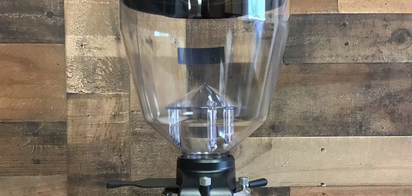 A large, clear plastic hopper with a black lid and metal base from the Mazzer Kony S Time-Based Commercial Espresso Coffee Grinder is wall-mounted—ideal for busy commercial environments. © 2025 1st-line.com