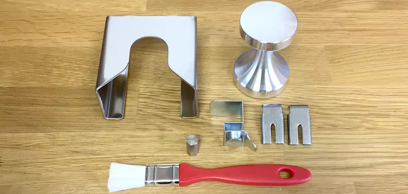 Metal coffee tools and accessories—including a tamper, portafilter holder, red-handled group head brush, and parts for the Mazzer Kony S Time-Based Commercial Espresso Coffee Grinder—are arranged on a wooden surface. © 2025 1st-line.com