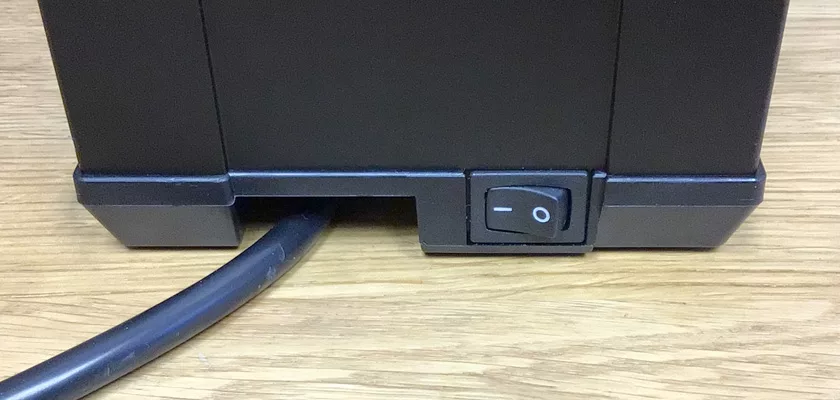 A close-up of the Macap Leo 55 Espresso Coffee Grinder shows its black power switch with on/off positions and a black power cord plugged in, while the grinder rests on a wooden surface. © 2025 1st-line.com