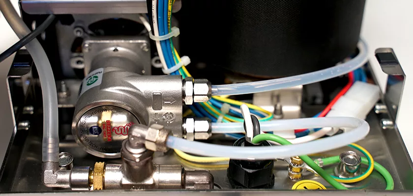 Close-up of internal components in the Bezzera Aria HX Special Edition Espresso Machine w/ Flow Control, including metal pipes, clear plastic tubes, electrical wires, a flow control pressure regulator, and various connectors. © 2025 1st-line.com