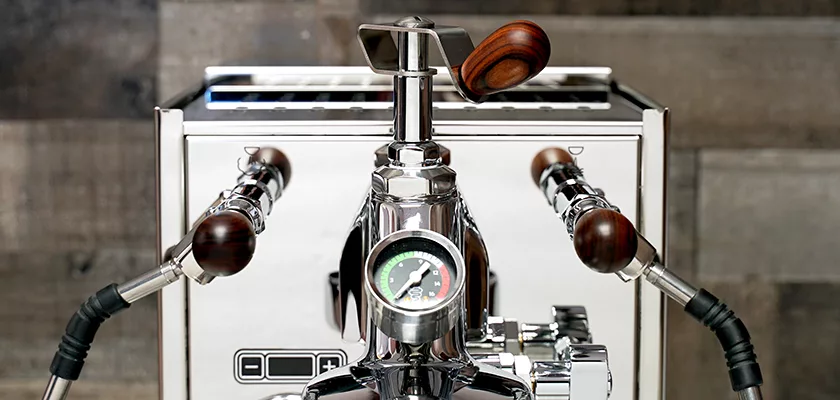 Close-up of the Bezzera Aria HX Special Edition Espresso Machine with flow control, wooden-handled levers, a central pressure gauge, and a metallic exterior, set against a wooden background. © 2025 1st-line.com