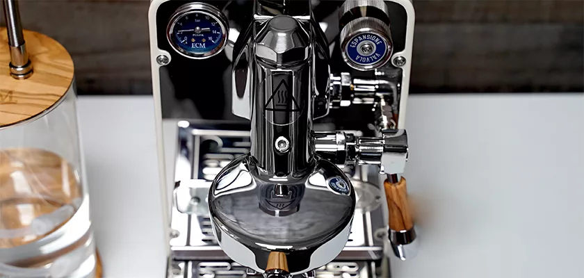 Close-up top view of the DISCONTINUED ECM Puristika Espresso Machine with chrome and wooden accents, pressure gauges, and a glass water reservoir on the left, displayed on a white surface. © 2025 1st-line.com
