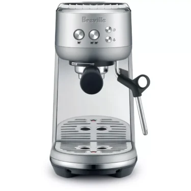 The Breville Bambino™ Espresso Machine in silver, featuring a steam wand, drip tray, control buttons, and portafilter holder, is shown from the front against a white background. © 2025 1st-line.com