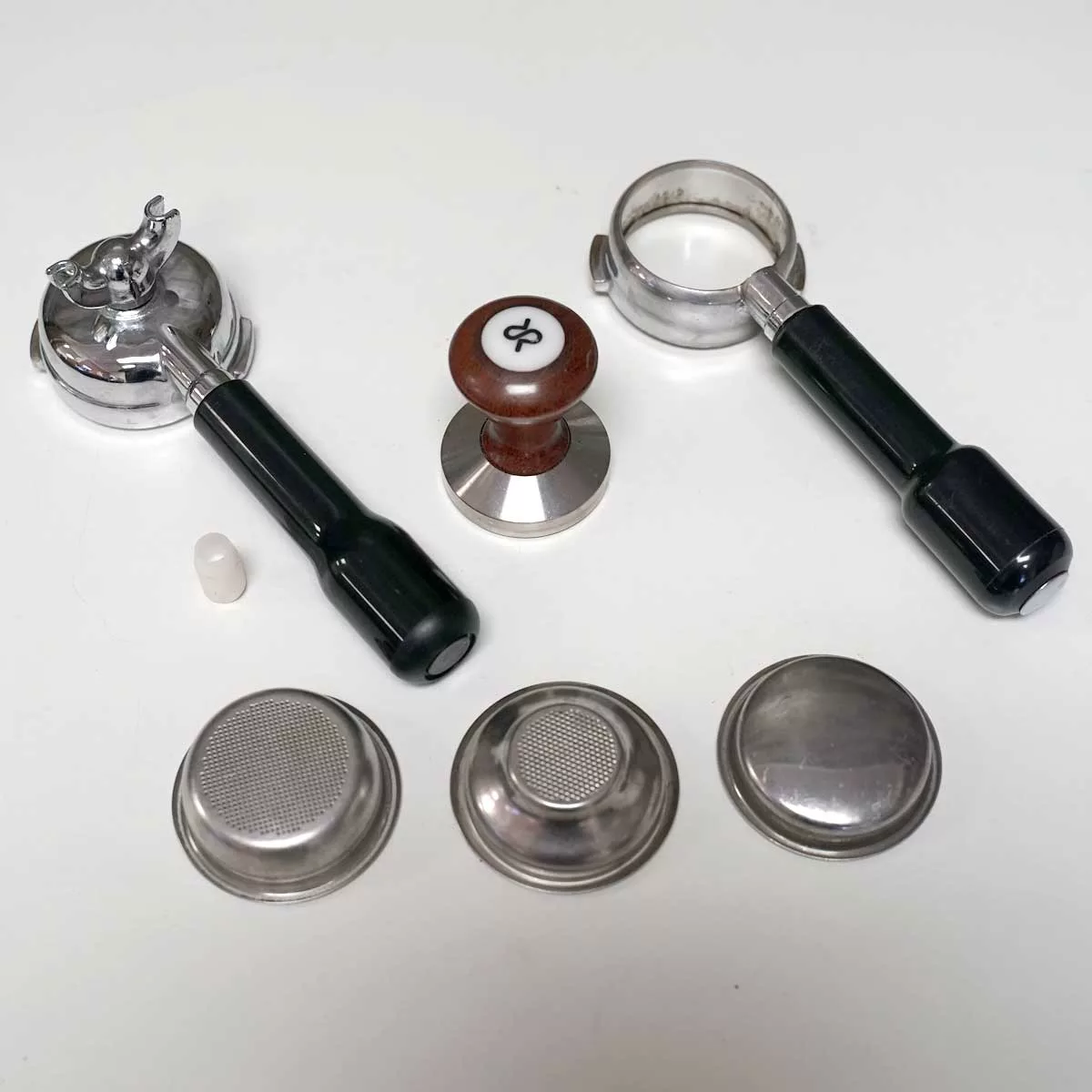 Accessories for the SIDEWALK SALE - Pasquini Livia 90 Electronic Espresso Machine USED (E113)—two espresso portafilters, a tamper, and metal filter baskets—are displayed on a white surface. © 2025 1st-line.com