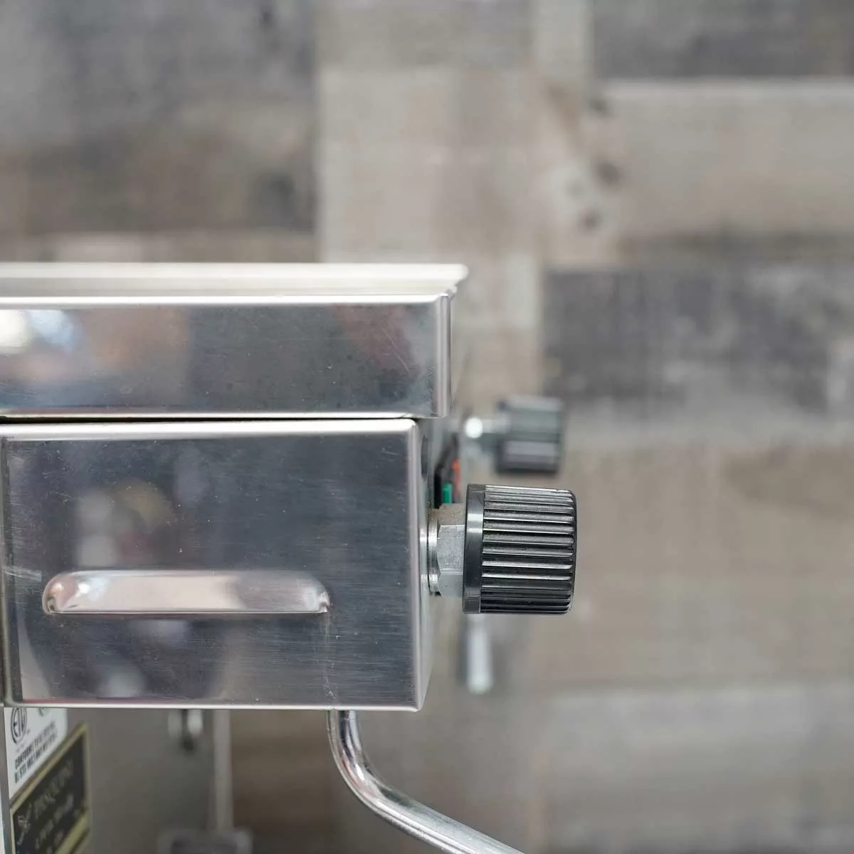 Close-up of a used SIDEWALK SALE - Pasquini Livia 90 Electronic Espresso Machine (E113) with stainless steel finish, black control knob and handle, set against a gray-tiled wall background. © 2025 1st-line.com