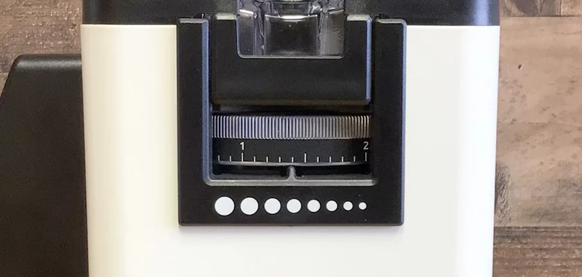Close-up of the Rancilio Stile Espresso Coffee Grinder, featuring a black grind size adjustment dial numbered 1 and 2 with white dots below it on the front panel, set against a wooden surface background. © 2025 1st-line.com