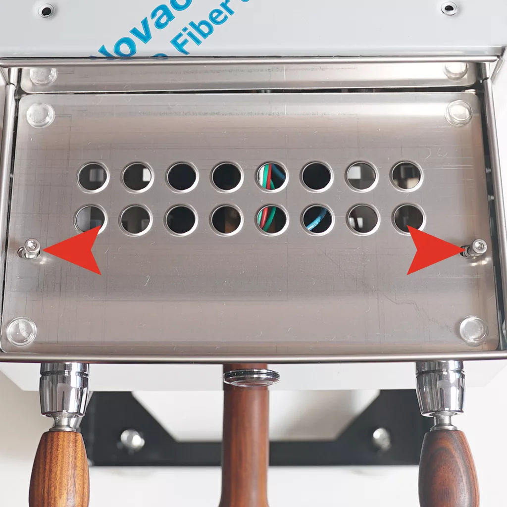 A close-up of a Bezzera Crema PM metal panel with circular holes, two red arrows pointing to screws on either side, and three wooden handles visible at the bottom. Colored wires are slightly visible through the holes. © 2025 1st-line.com