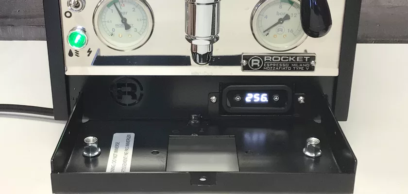 A close-up of the Rocket Mozzafiato Cronometro Type V HX Espresso Machine highlights its pressure gauges, green power indicator, a digital PID temperature display showing 256, and an open front compartment revealing internal parts. © 2025 1st-line.com