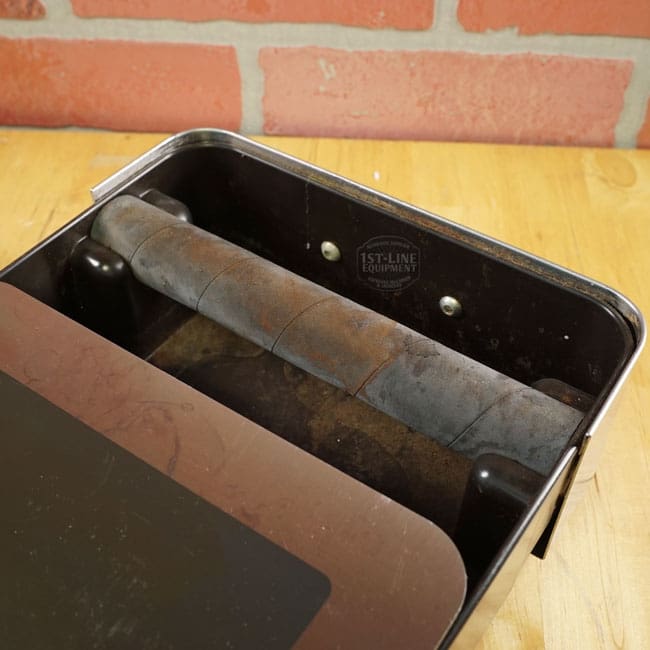 A close-up of the SIDEWALK SALE - Lelit PLA360M Knock Box Drawer (E208), featuring a black rubber bar and slight wear, sits on wood with a red brick backdrop—ideal for bargain hunters at your next sidewalk sale. © 2025 1st-line.com