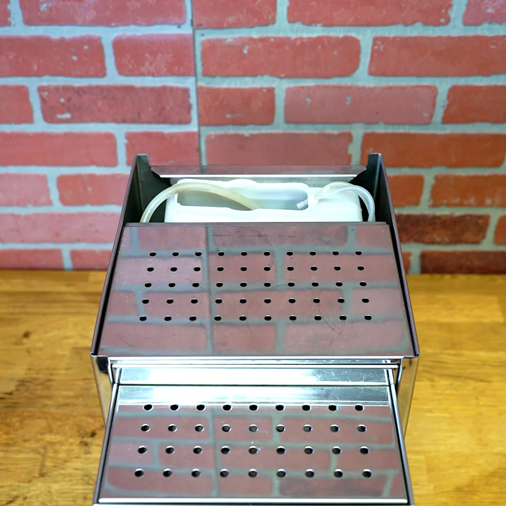 A (SOLD) SIDEWALK SALE - Pasquini Livia G4 PID Electronic Espresso Machine (USED) with a perforated stainless steel top and front sits on a wooden counter against a red brick wall, with its white power cord coiled neatly on top. © 2025 1st-line.com