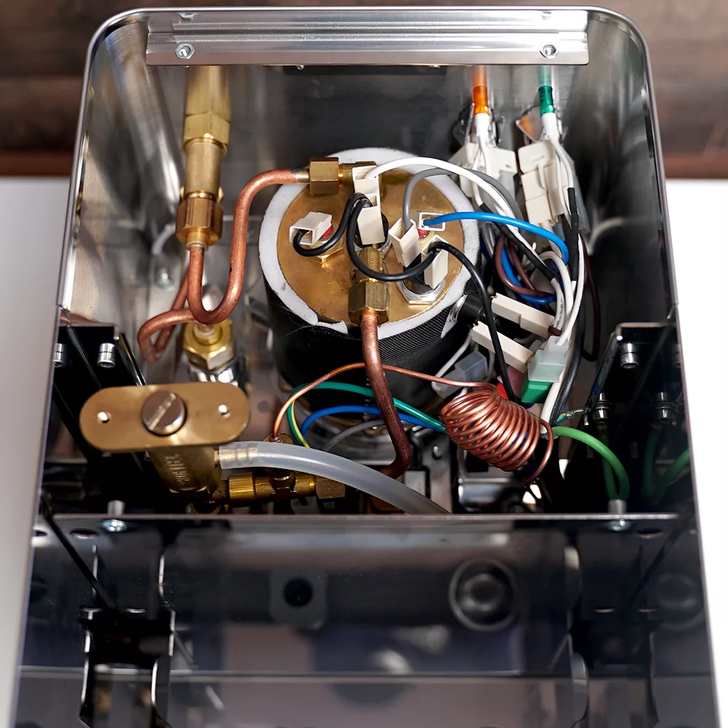 Accessing the inside of the ECM Casa V reveals internal components, including a large metal boiler, copper pipes, various wires, connectors, tubes, and electronic parts within a reflective metal casing. © 2025 1st-line.com