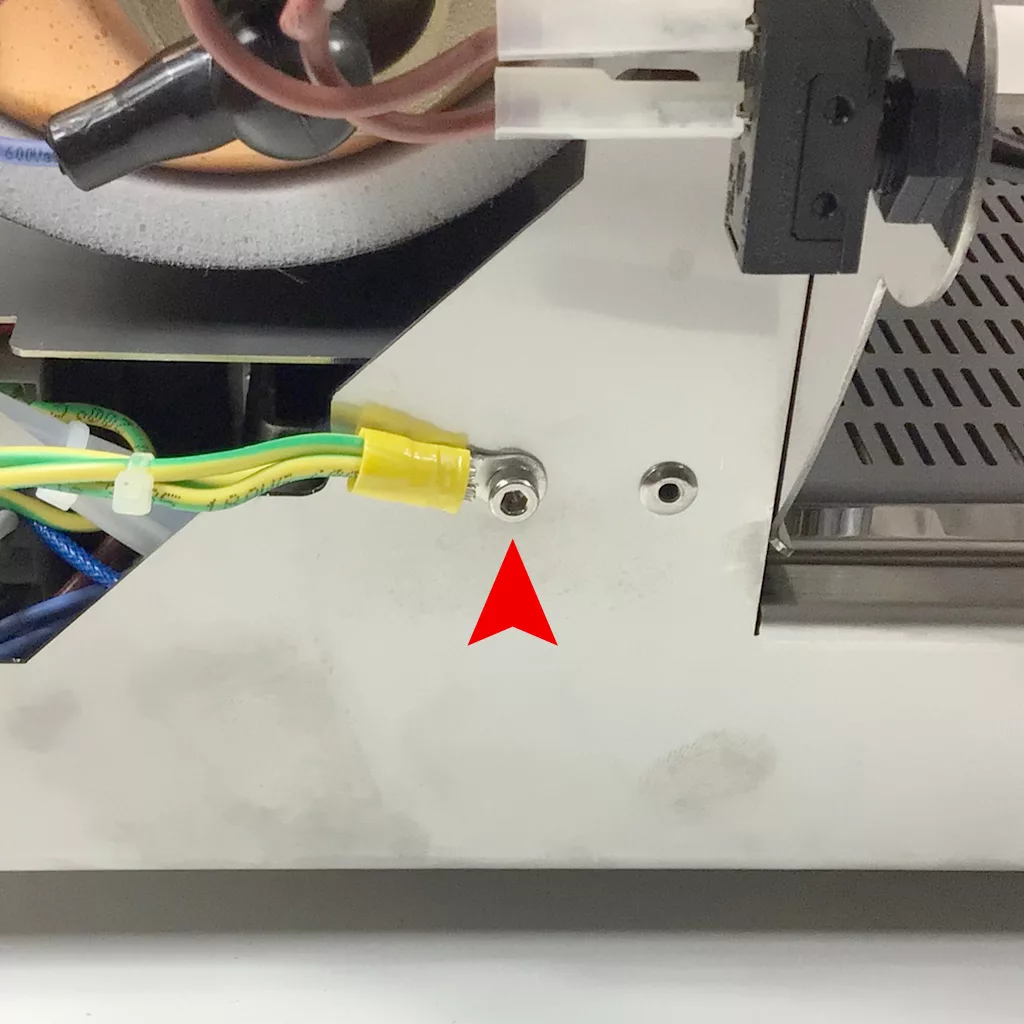 Close-up of a Cuadra metal device with wires attached and a red arrow pointing to a small metal screw or connector on a white panel, indicating where accessing the inside may be required. © 2025 1st-line.com