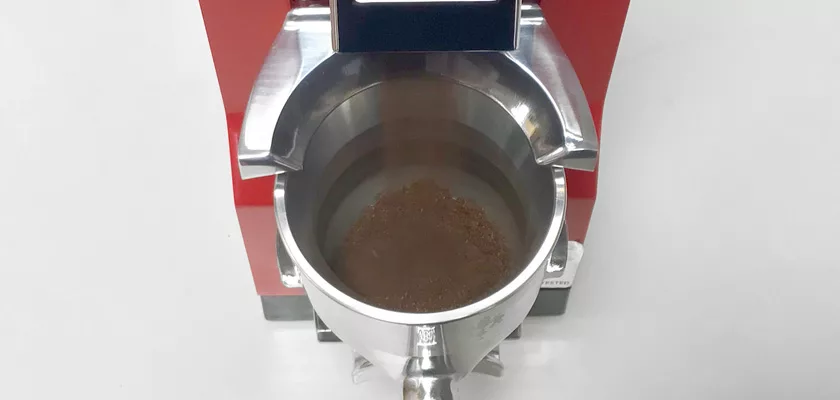 Close-up of a metal container on a red espresso machine, filled with freshly ground coffee from the Eureka Mignon Libra Espresso Coffee Grinder – Weight-Based Grinding, ensuring perfect brewing. © 2025 1st-line.com