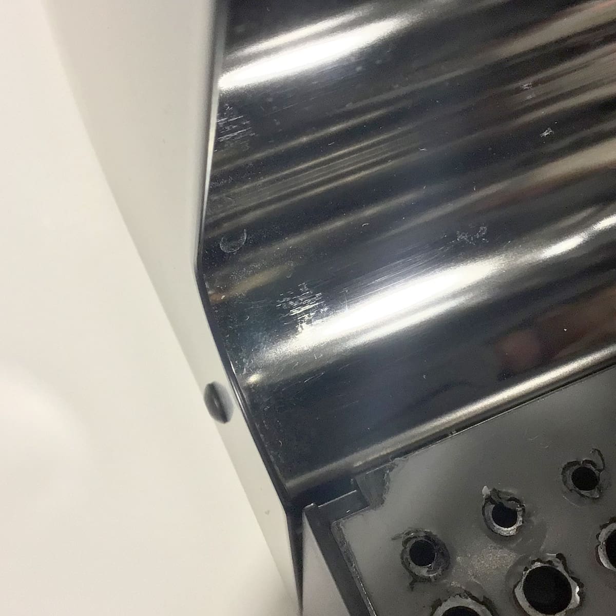 Close-up of a metallic hand dryer with a shiny surface next to a black panel with round holes, similar to the vent or drip tray on the SIDEWALK SALE VBM Domobar Junior Digital HX Espresso Machine w/ Flow Control (OPEN BOX) (E014). © 2025 1st-line.com