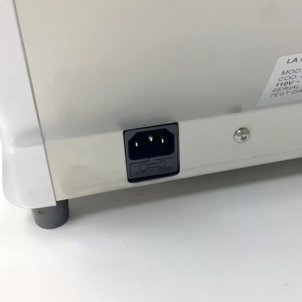 Close-up of the back of a Cuadra electronic device showing a three-prong power connector socket and part of a product label, with a white and gray casing, black foot, and hints for accessing the inside. © 2025 1st-line.com