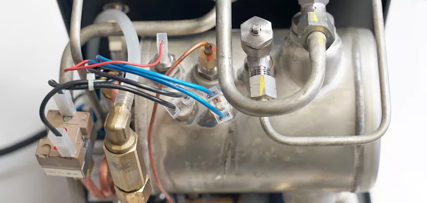 Close-up of the Rocket Appartamento TCA HX Espresso Machine boiler, showcasing metal pipes, wiring, and connectors essential for heating and water distribution within the TCA HX system. © 2025 1st-line.com