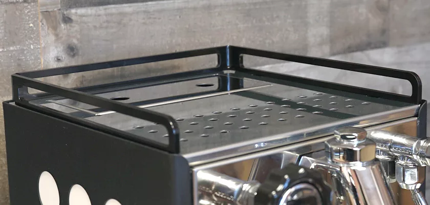 Close-up of the Rocket Appartamento TCA HX Espresso Machine showing its metal rail and perforated tray, set against a wood-paneled background. © 2025 1st-line.com