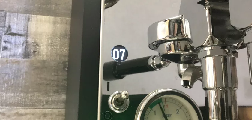 Close-up of the Rocket Mozzafiato Cronometro Type V HX Espresso Machine, highlighting its digital display showing 07, pressure gauge, lever, and metallic HX components against a textured wooden background. © 2025 1st-line.com