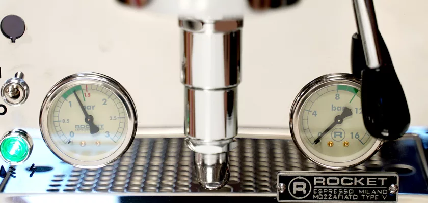 Close-up of the Rocket Mozzafiato Cronometro Type V HX Espresso Machine’s front panel, showing dual pressure gauges, a metal drip tray, a green indicator light, and the portafilter handle underneath. © 2025 1st-line.com