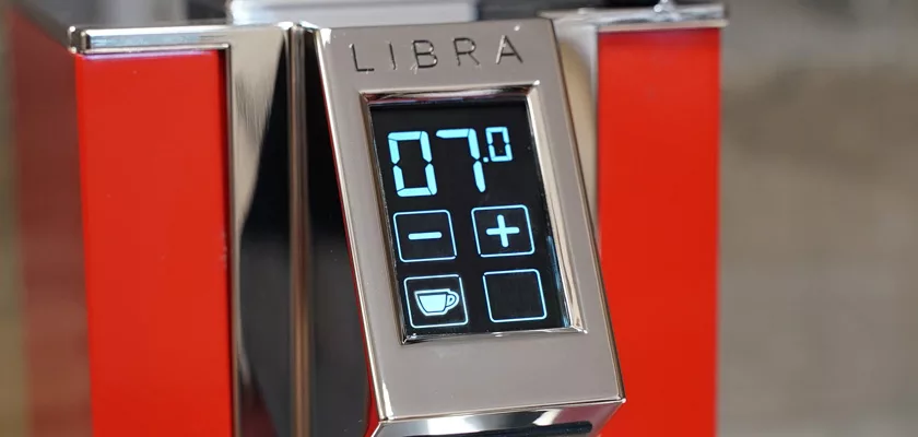 Close-up of the shiny metal Eureka Mignon Libra Espresso Coffee Grinder - Weight-Based Grinding control panel labeled LIBRA, with a digital display showing 07 and plus, minus, and coffee cup buttons, set against a red background. © 2025 1st-line.com