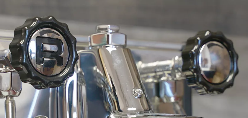 Close-up of two black faucet handles with chrome accents on a Rocket Appartamento TCA HX Espresso Machine; the left handle displays a raised R. The blurred background emphasizes the machines shiny metal and detailed fixtures. © 2025 1st-line.com