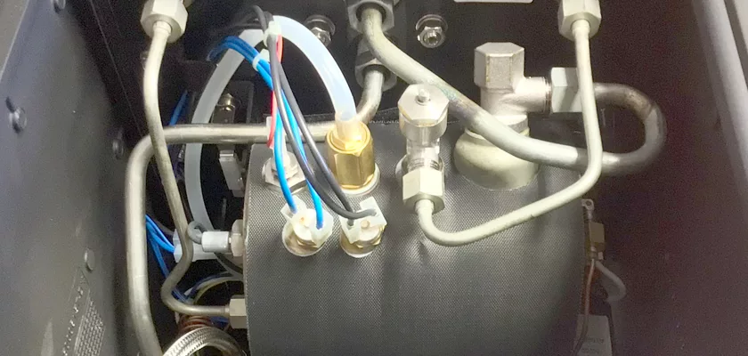 Close-up view inside the Rocket Mozzafiato Cronometro Type V HX Espresso Machine reveals metal pipes, wires, connectors, a black cylindrical tank, and fittings neatly arranged within the compact interior. © 2025 1st-line.com