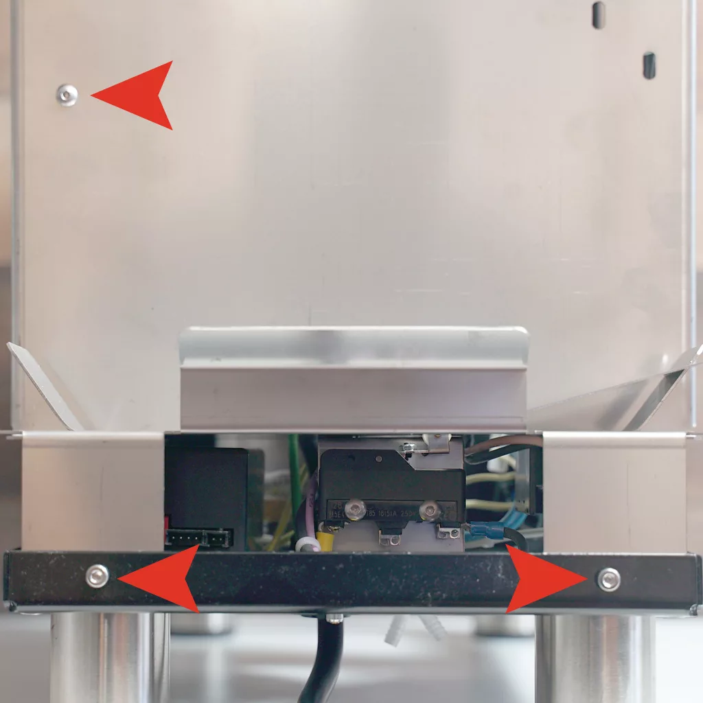 Close-up view of a Bezzera Crema PM lower back panel, with three red arrows highlighting screws and components; wiring and metal legs can be seen partially below. © 2025 1st-line.com