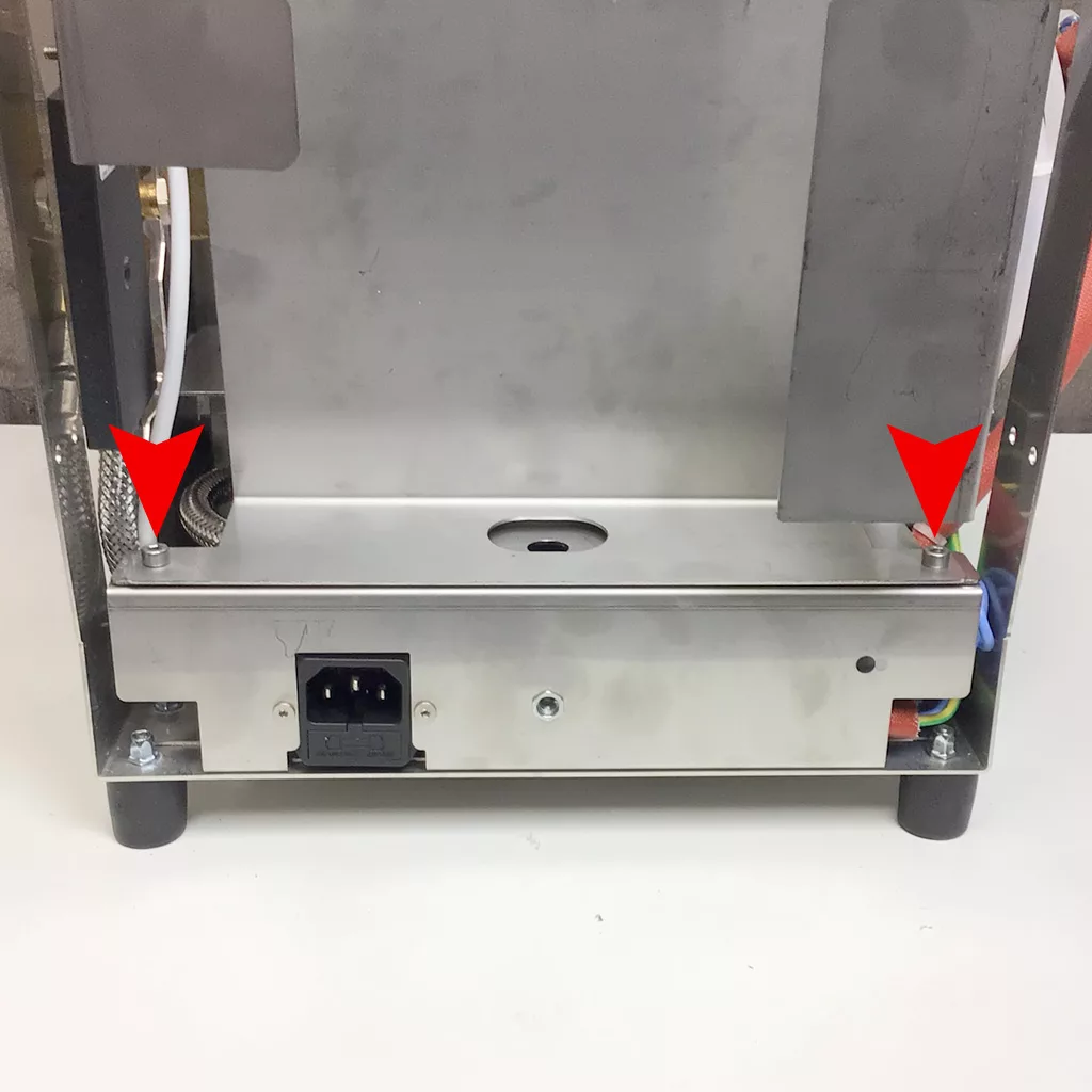 Rear view of a Cuadra metal appliance with two red arrows pointing to screws on either side of a panel, indicating where to unscrew for accessing the inside. An electrical socket and cables are visible at the bottom. © 2025 1st-line.com