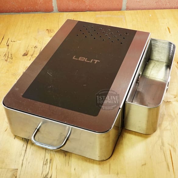 The SIDEWALK SALE - Lelit PLA360M Knock Box Drawer (E208), featuring stainless steel and a black top cover, is perfect for espresso grounds disposal—displayed on wood against a brick wall for your next sidewalk sale. © 2025 1st-line.com