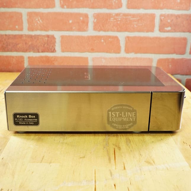 The SIDEWALK SALE - Lelit PLA360M Knock Box Drawer (E208) with a transparent lid rests on wood before a red brick wall, labeled Knock Box PL120 - Made in Italy and 1st-Line Equipment. Ideal for your Sidewalk Sale espresso setup. © 2025 1st-line.com