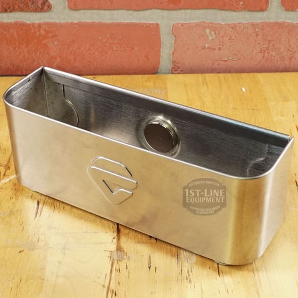 The SIDEWALK SALE - Lelit PLA360M Knock Box Drawer (E208) with rounded edges and a front logo rests on wood before a brick wall—its stainless steel build and circular indentation make it an ideal display piece. © 2025 1st-line.com