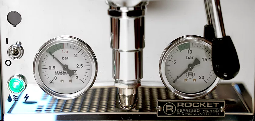 Close-up of a Rocket Espresso machine control panel showing two pressure gauges, an illuminated green power button, and a metallic steam wand, with the Rocket branding visible at the bottom. © 2025 1st-line.com