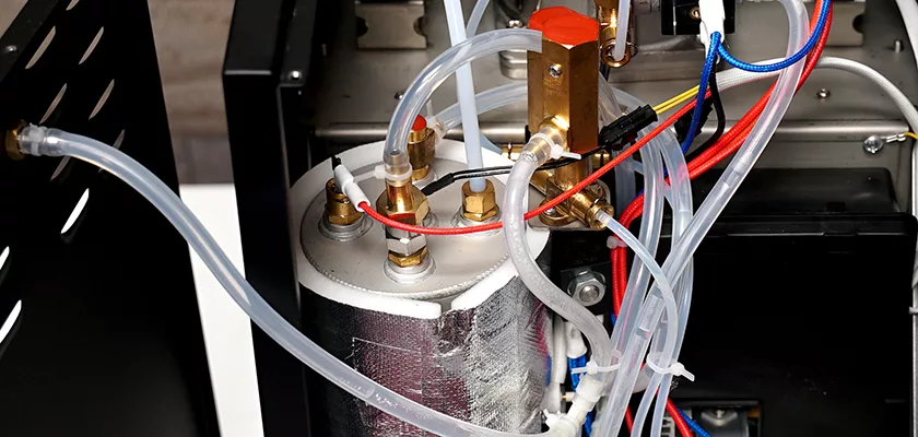 Close-up of the Bellezza Bellona Dual Boiler Espresso Machine interior, revealing metal parts, tubing, wiring, a cylindrical water boiler, and connectors in a compact technical arrangement. © 2025 1st-line.com