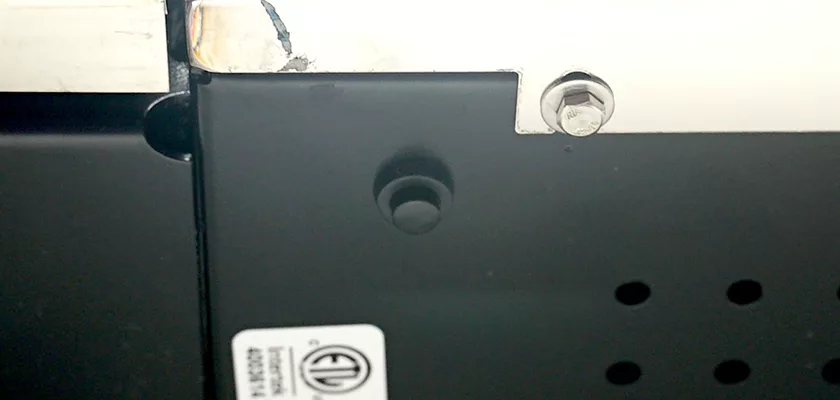 Close-up of the black and white metal surface of the Rocket Giotto Cronometro Type V HX Espresso Machine, showing a bolt, small round button, scratches, and a partially visible ETL certification label at the bottom left. © 2025 1st-line.com