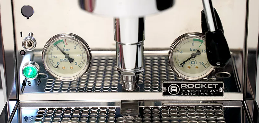 Close-up of the Rocket Giotto Cronometro Type V HX Espresso Machine’s front panel, showing two pressure gauges, indicator lights, a metal grate, and the Cronometro Type V nameplate. © 2025 1st-line.com