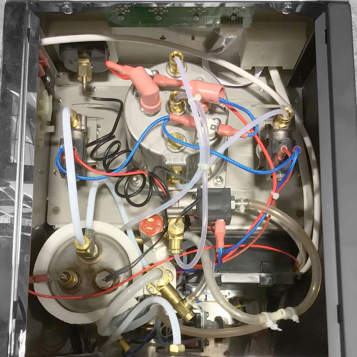 The interior of the Bellezza Bellona Dual Boiler Espresso Machine features a compact, technical layout with colored electrical wires, white and clear plastic tubes, metal fittings, and various components neatly arranged. © 2025 1st-line.com