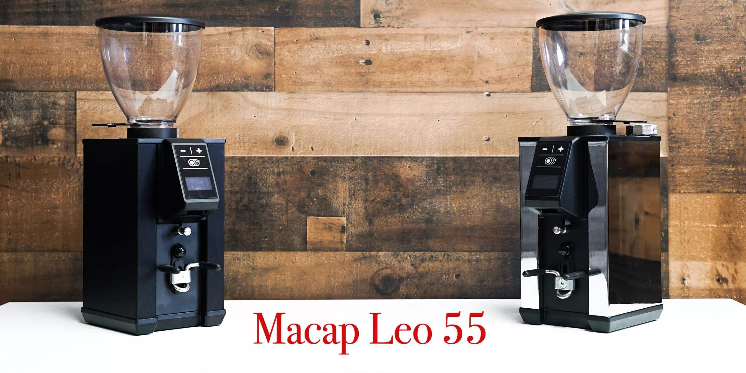Two premium black Macap Leo 55 coffee grinders are placed on a white surface in front of a wooden wall. The words Macap Leo 55 appear in red text at the bottom of the image. © 2025 1st-line.com