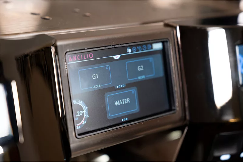 A close-up of the digital touchscreen on the Rancilio Invicta 2 Group Commercial Espresso Machine displays buttons labeled G1, G2, and WATER, all framed by glossy black trim. © 2025 1st-line.com