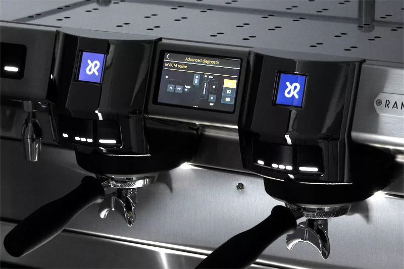Close-up of the Rancilio Invicta 2 Group Commercial Espresso Machine, featuring two portafilters, a digital touchscreen with diagnostics, and blue illuminated buttons on a sleek metallic background. © 2025 1st-line.com