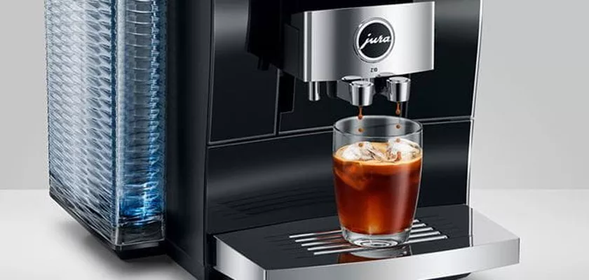 The Jura Z10 Super-Automatic Espresso Machine pours coffee over ice into a clear glass on its drip tray, with the water reservoir visible on the left. © 2025 1st-line.com
