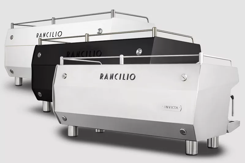 Three Rancilio Invicta 2 Group Commercial Espresso Machines—shown in white, black, and gray—are arranged in a staggered row on a simple light background, showcasing their modern design and robust metal feet. © 2025 1st-line.com