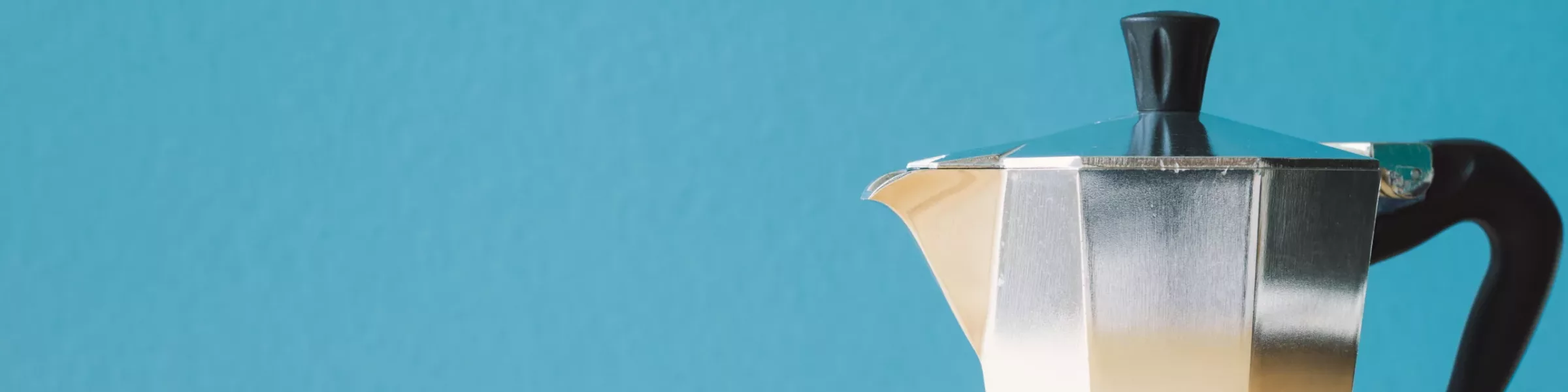 A close-up of a silver stovetop Coffee Maker with a black handle and knob, set against a plain blue background. Only the upper right portion of the espresso maker is visible. © 2025 1st-line.com