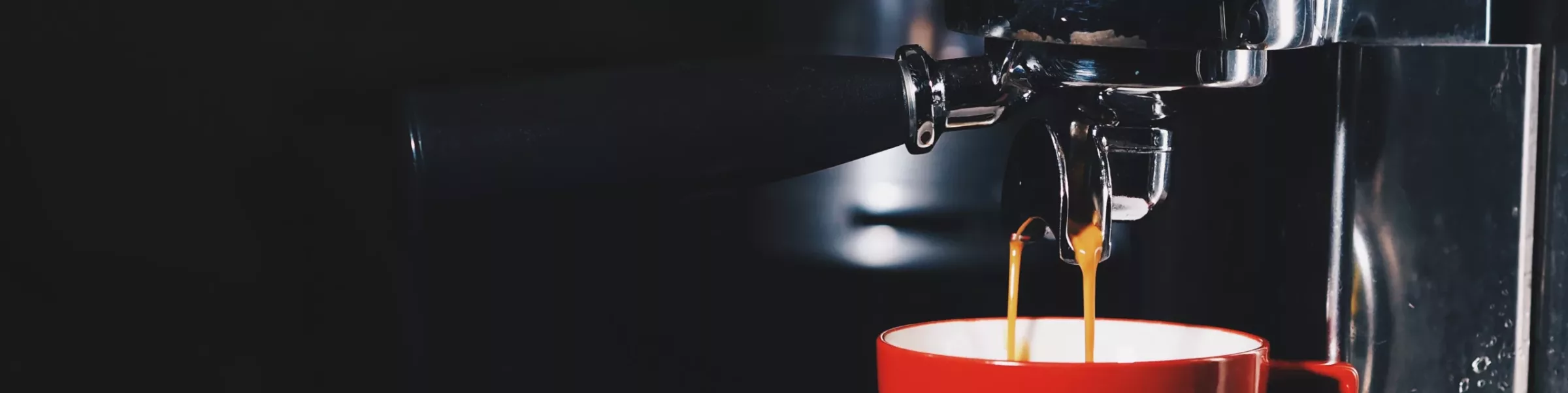 Close-up of an espresso machine from our Shop All Espresso Machines range, pouring coffee into a red cup, with a dark background highlighting the coffee streams and shiny metal parts. © 2025 1st-line.com