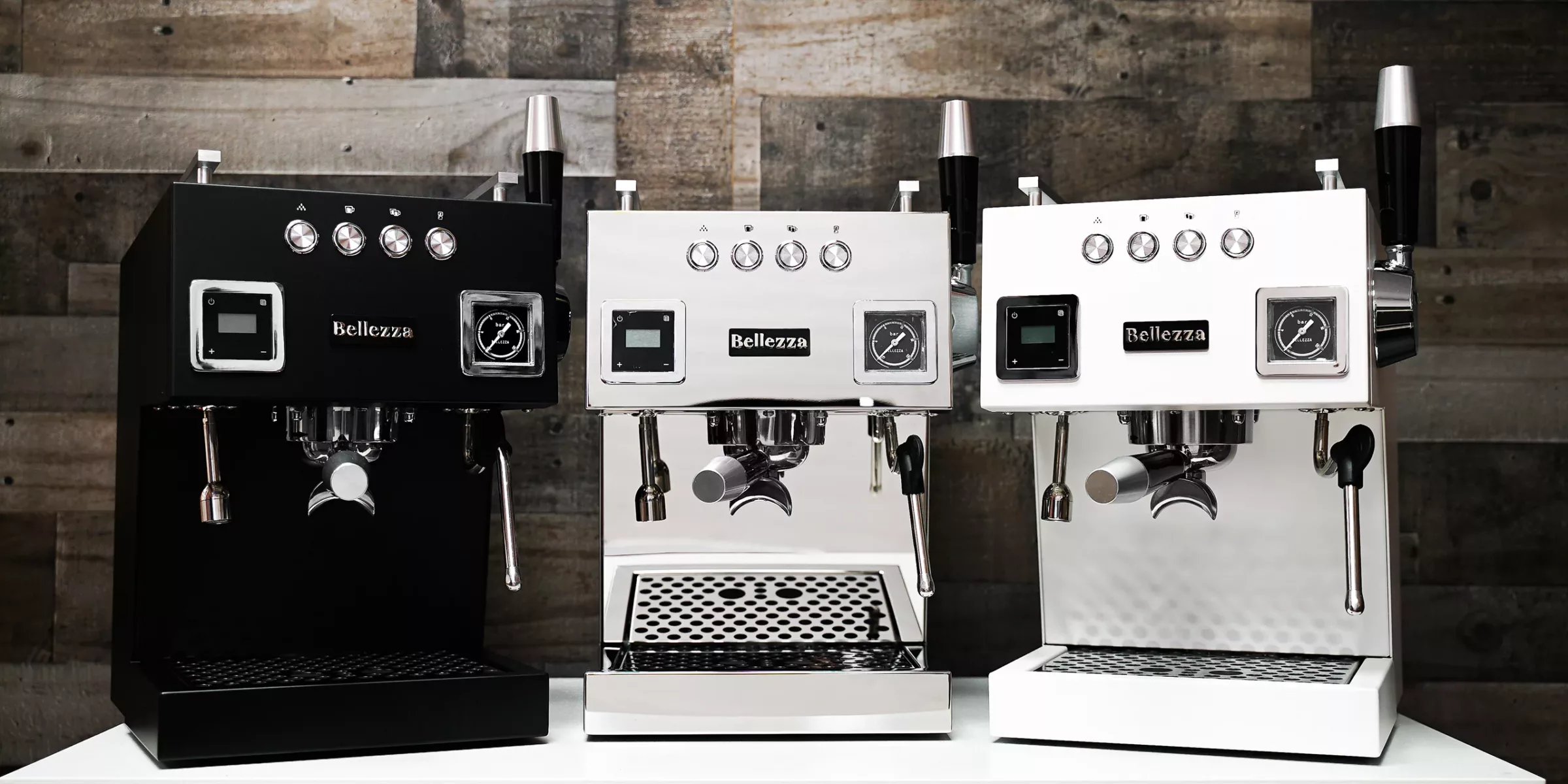 Three Bellezza espresso machines—one black, one chrome, and one white—are displayed side by side on a white counter against a rustic wooden background, making the perfect gift for Mother’s Day. © 2025 1st-line.com